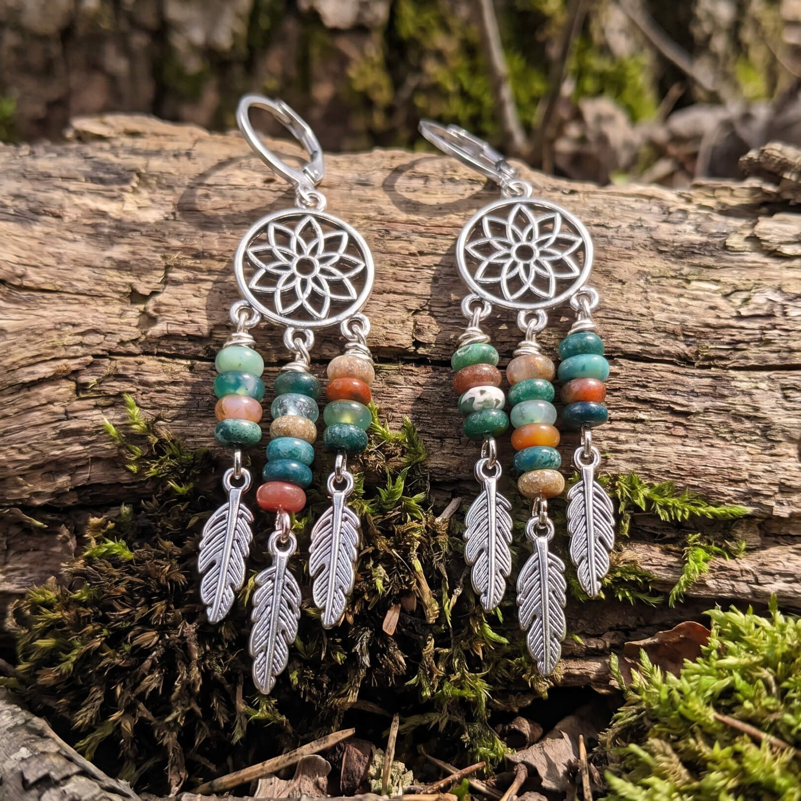Silver dreamcatcher earrings with fancy jasper beads and feathers on a log